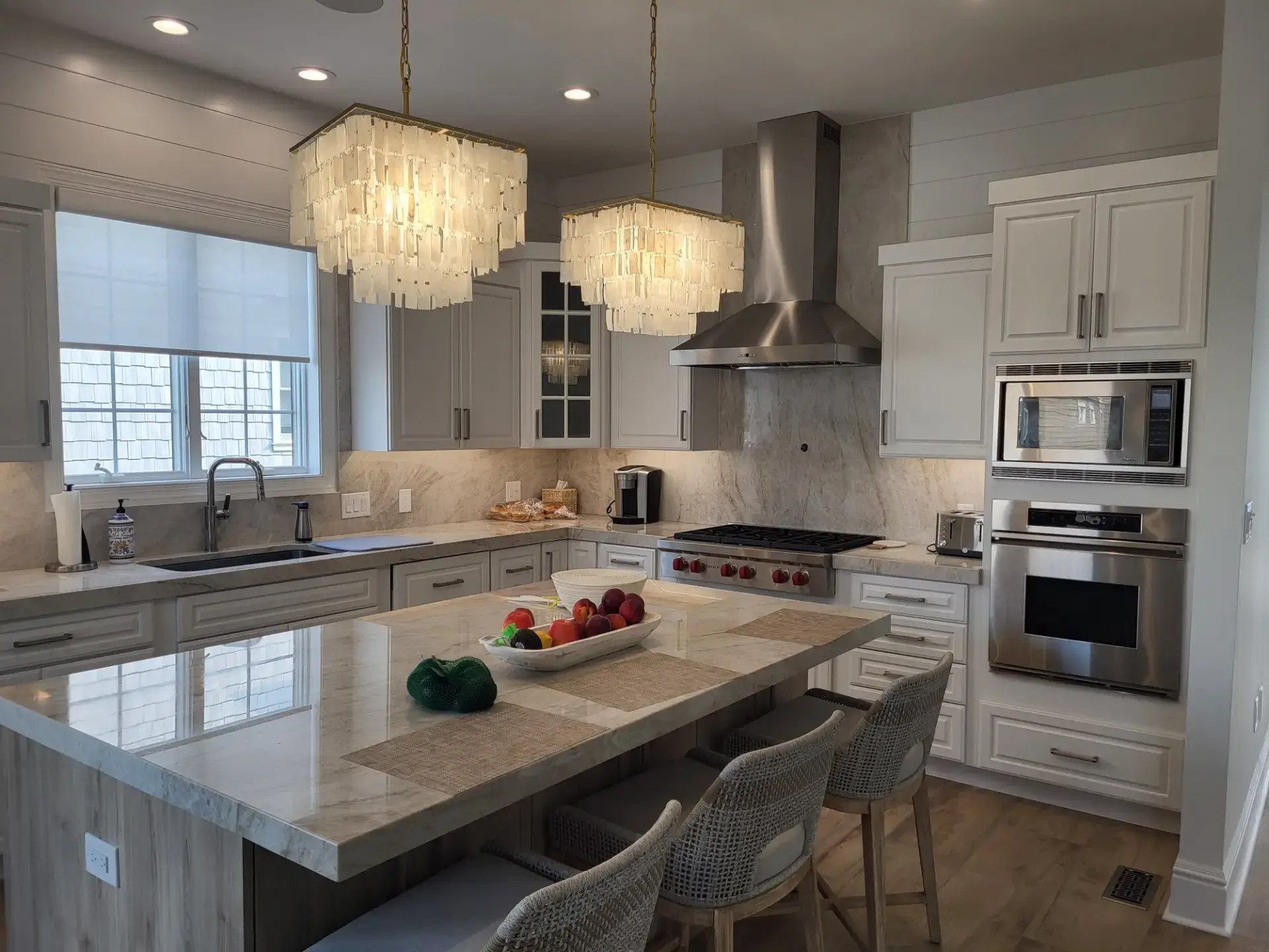 Veined stone island under tiered chandeliers in a white kitchen